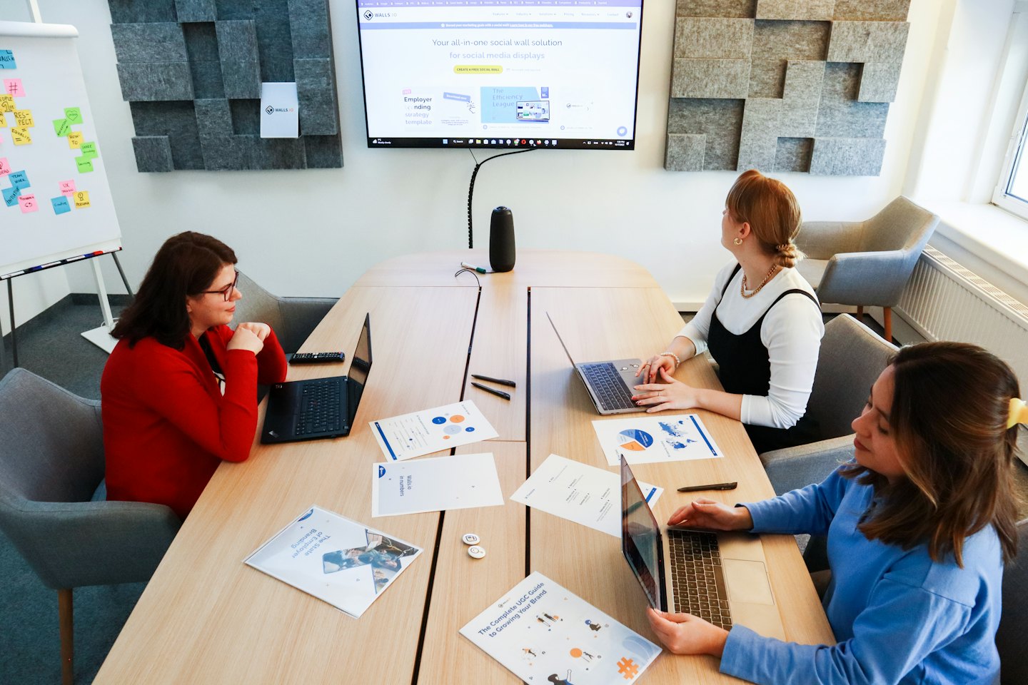 Three women work together on laptops at an office table.